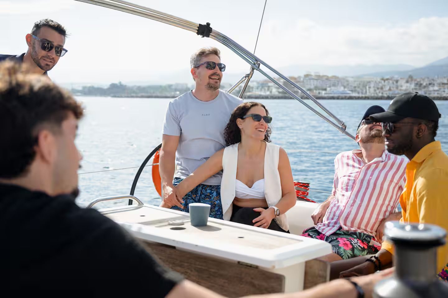 Group of friends enjoying a private sailing yacht charter in Marbella, with Puerto Banús in the background