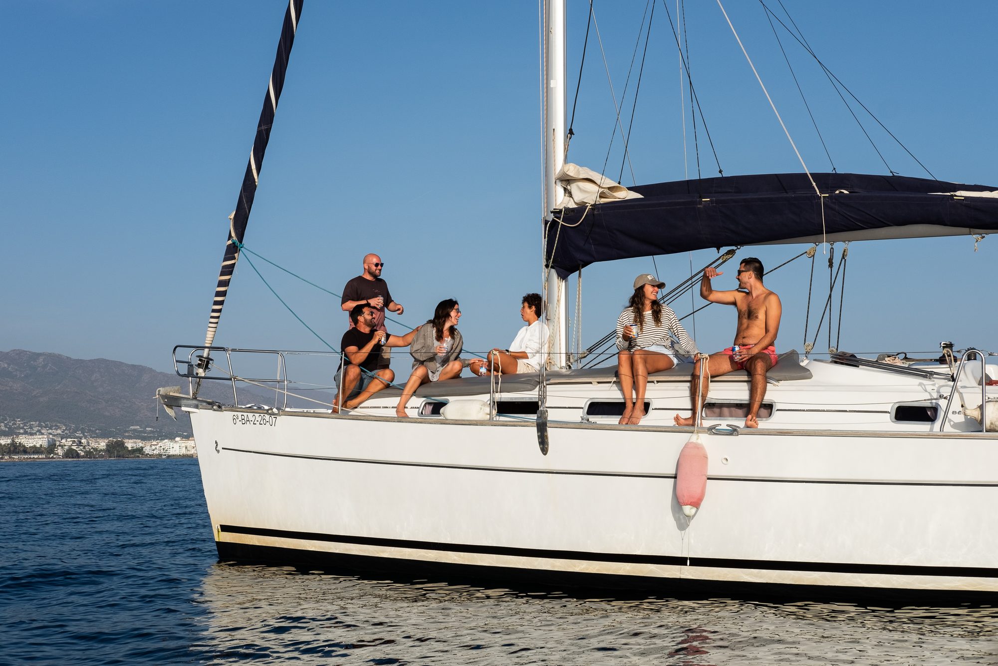 Group enjoying a shared sailing trip on deck off Puerto Banús, Marbella